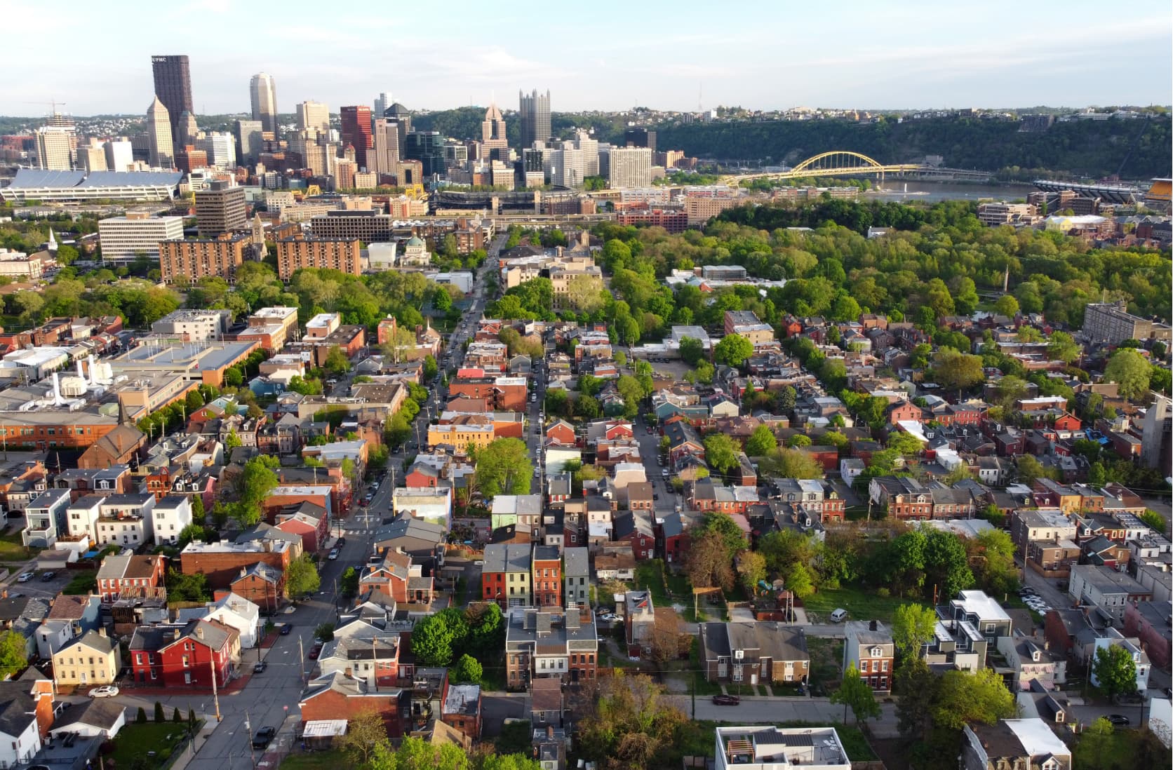 Aerial view of a Pittsburgh rowhouse neighborhood with the downtown skyline and river beyond
